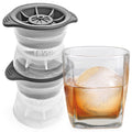 A set of two tovolo Sphere Ice Molds sits beside a glass of whiskey containing a perfectly shaped, slow-melting ice sphere created by the molds.