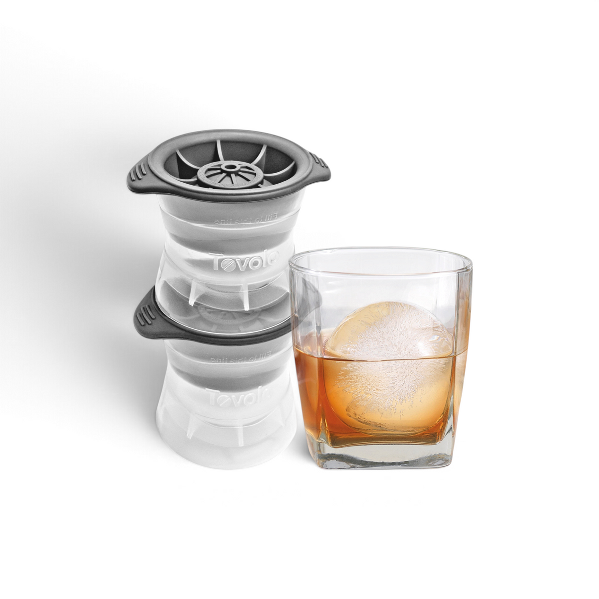 A set of two tovolo Sphere Ice Molds sits beside a glass of whiskey containing a perfectly shaped, slow-melting ice sphere created by the molds.