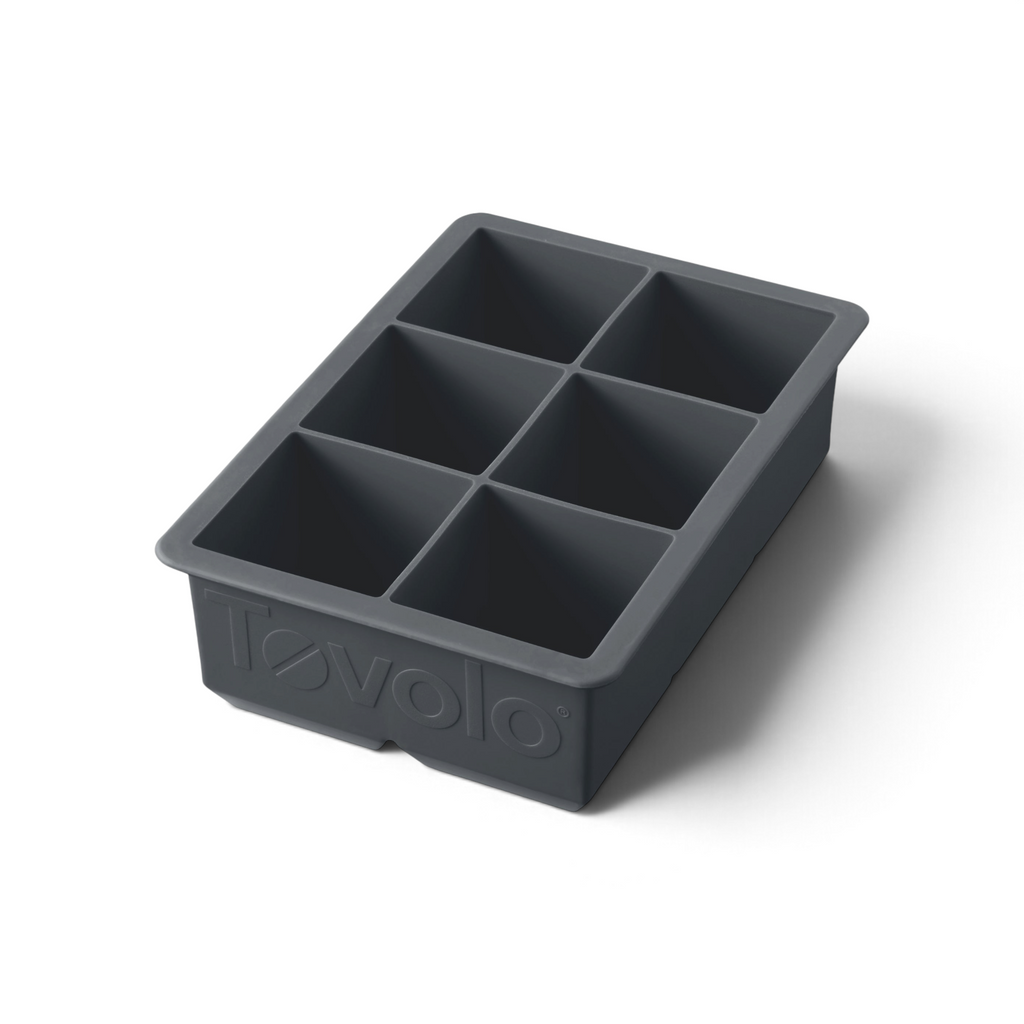 The tovolo King Cube Silicone Ice Mold is a black tray with six large square compartments, ideal for crafting big ice cubes. The word "tovolo" is embossed on the front of this craft ice mold.