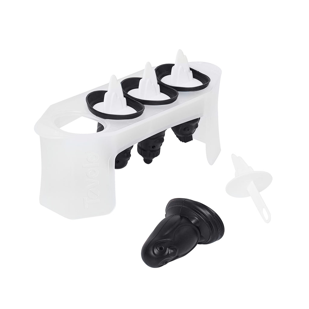 The Penguin Pop Molds set features a slimline tray holding four black and white molds shaped like penguins, with one mold removed and its white stick beside it—ideal for crafting homemade frozen treats.