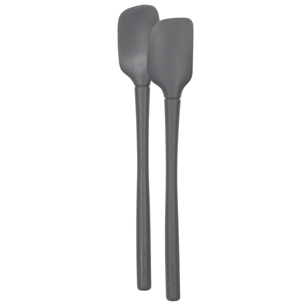 The Flex-Core Mini Spat + Spoonula, two gray heat-resistant silicone kitchen utensils, stand upright side by side against a white background.