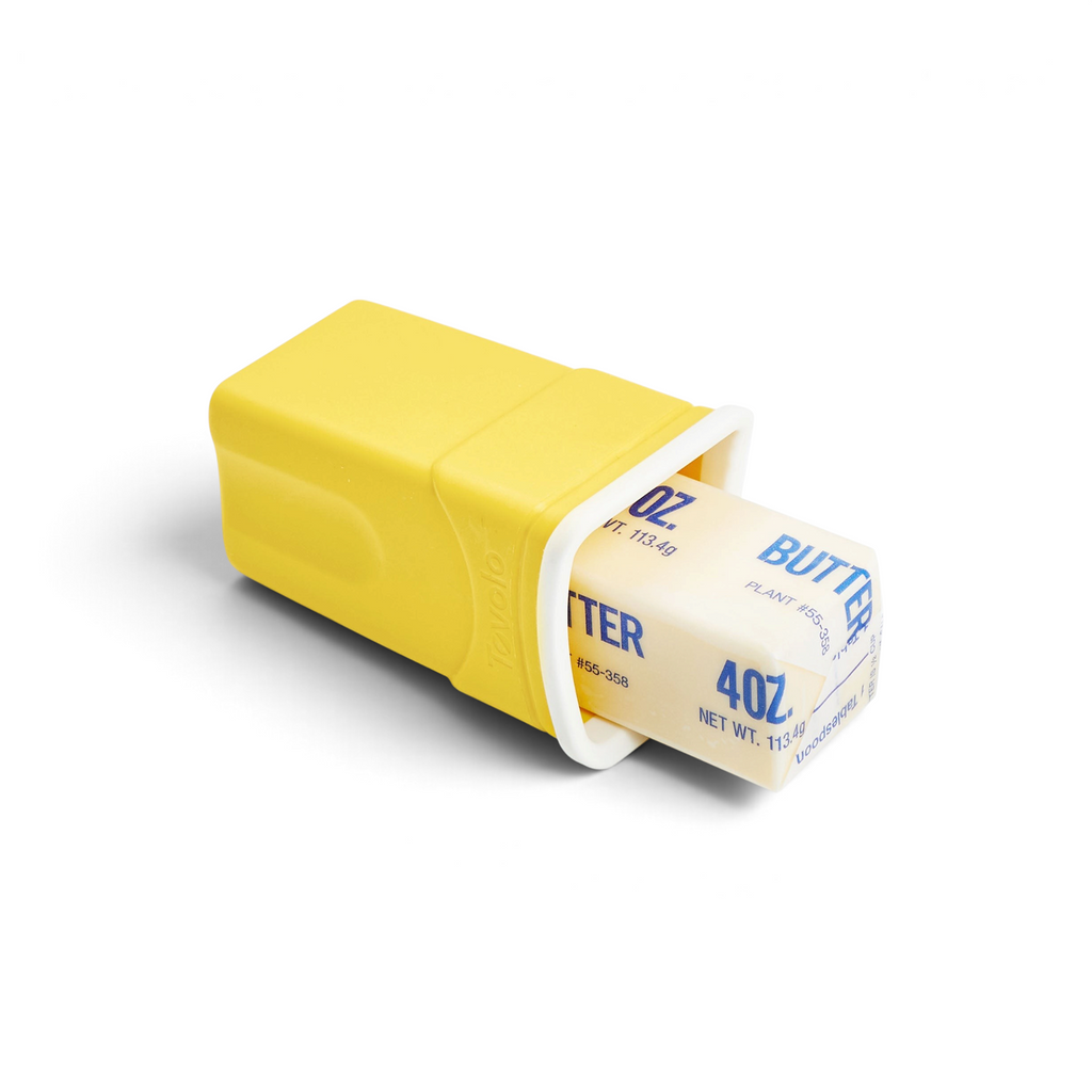 The Butter Sleeve, in yellow, securely holds a stick of butter—partially slid out to show its label—for a clean, mess-free butter experience.