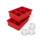 Two red tovolo King Cube Silicone Ice Molds (Set of 2), each with six large square compartments, are stacked. In front, three large clear craft ice cubes are displayed.