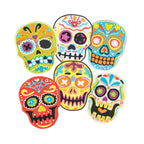 Six vibrant sugar skull cookies, made with Skull Cookie Cutters, are arranged on a white background—their colorful icing and Día de los Muertos-inspired patterns offer a festive twist reminiscent of classic holiday cookie designs.