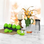 A marble countertop displays the Sphere Clear Ice Mold with bar-quality ice spheres, clear glasses with drinks, a stainless steel travel mug, a green vase with yellow flowers, and a white candle on a wooden stand.
