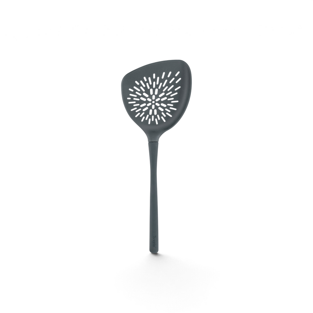 The Roasted Veggie Tool is a gray turner with a long handle and wide triangular head, featuring starburst holes for draining—ideal for serving roasted vegetables.