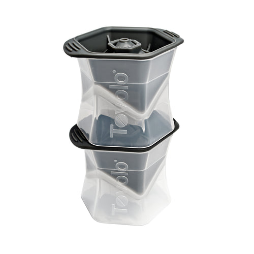 Two stacked tovolo Colossal Ice Molds (Set of 2) in clear and dark gray create large, geometric, slow-melting ice cubes. Each mold features the tovolo logo on the side.