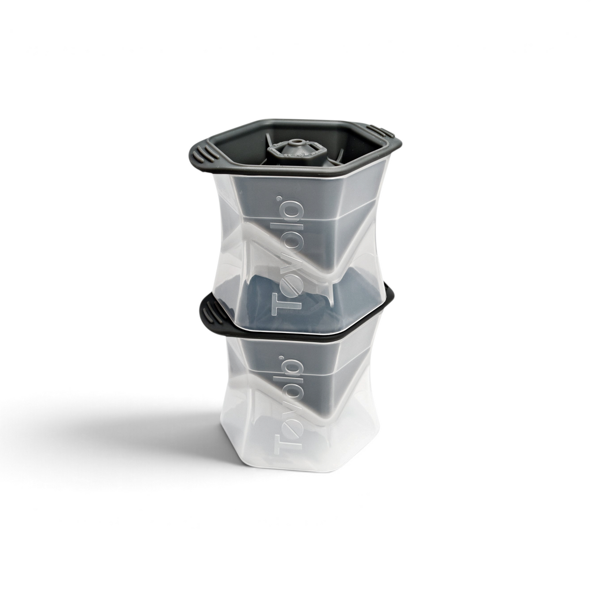Two stacked tovolo Colossal Ice Molds (Set of 2) in clear and dark gray create large, geometric, slow-melting ice cubes. Each mold features the tovolo logo on the side.
