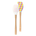 The Kitchen Hacks Spatulart set features a wood-handled spatula with a colorful fish scale design and a pink baking conversion spatula with measurement markings; both silicone spatulas include engraved logos near the base of the handles.