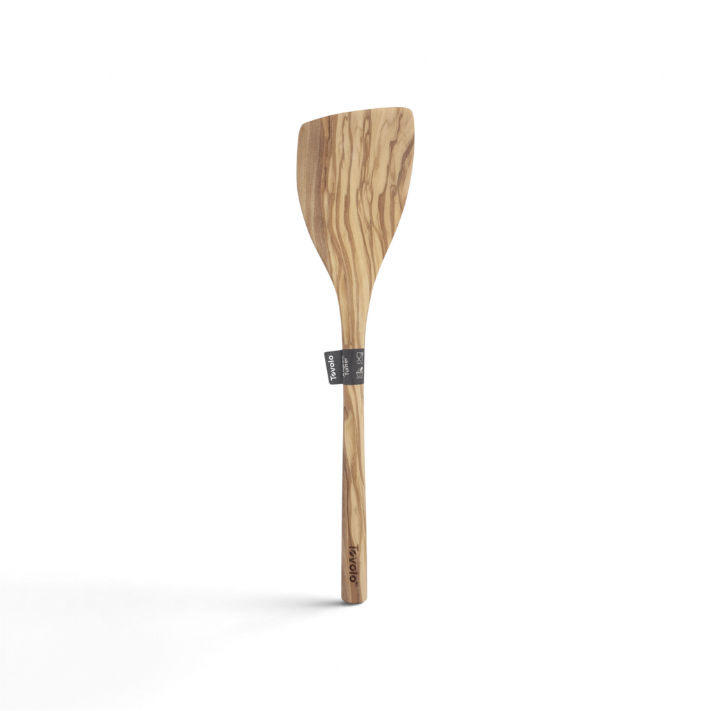The Olivewood Utensils feature a flat, angled head and long handle, with a natural wood grain and a small label. This nonstick-safe olivewood spatula doubles as an elegant pancake turner.