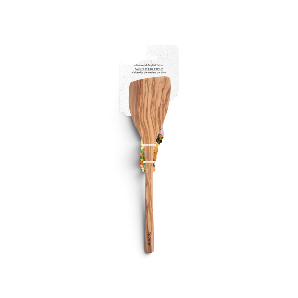 An Olivewood Utensils pancake turner in packaging is shown with a prepared, herb-garnished omelet in the background. The wooden spatula features a flat, wide blade, smooth handle, and is safe for nonstick cookware.