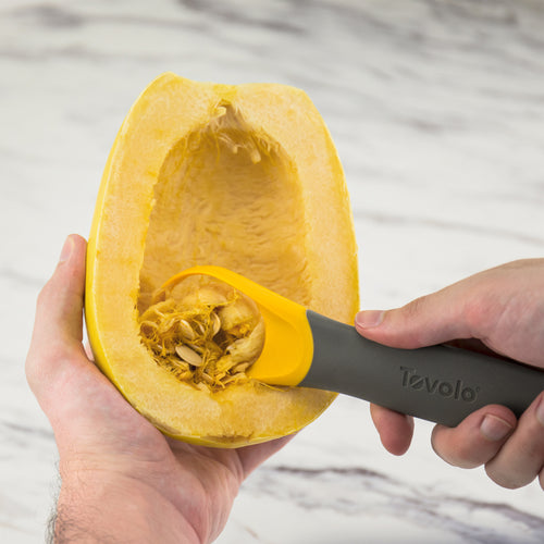 Using the 2-in-1 Squash Tool with its nylon blade, a person removes seeds from a halved spaghetti squash on a marble surface.