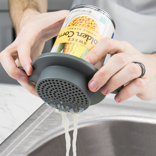 Using a Can Do Strainer, a person drains liquid from a can of sweet corn over a kitchen sink.