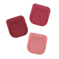 Three red and pink square silicone pan scrapers, each with an embossed owl face, are designed for cleaning non-stick bakeware or cast iron skillets.