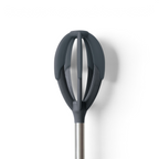 A close-up of the Better Batter Tool—a modern whisk with dark gray, oval silicone blades and a stainless steel handle—appears against a white background, ideal for mixing batters.