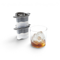 Tovolo pickleball-shaped silicone ice molds stacked next to a glass of whiskey with a pickleball ice sphere.